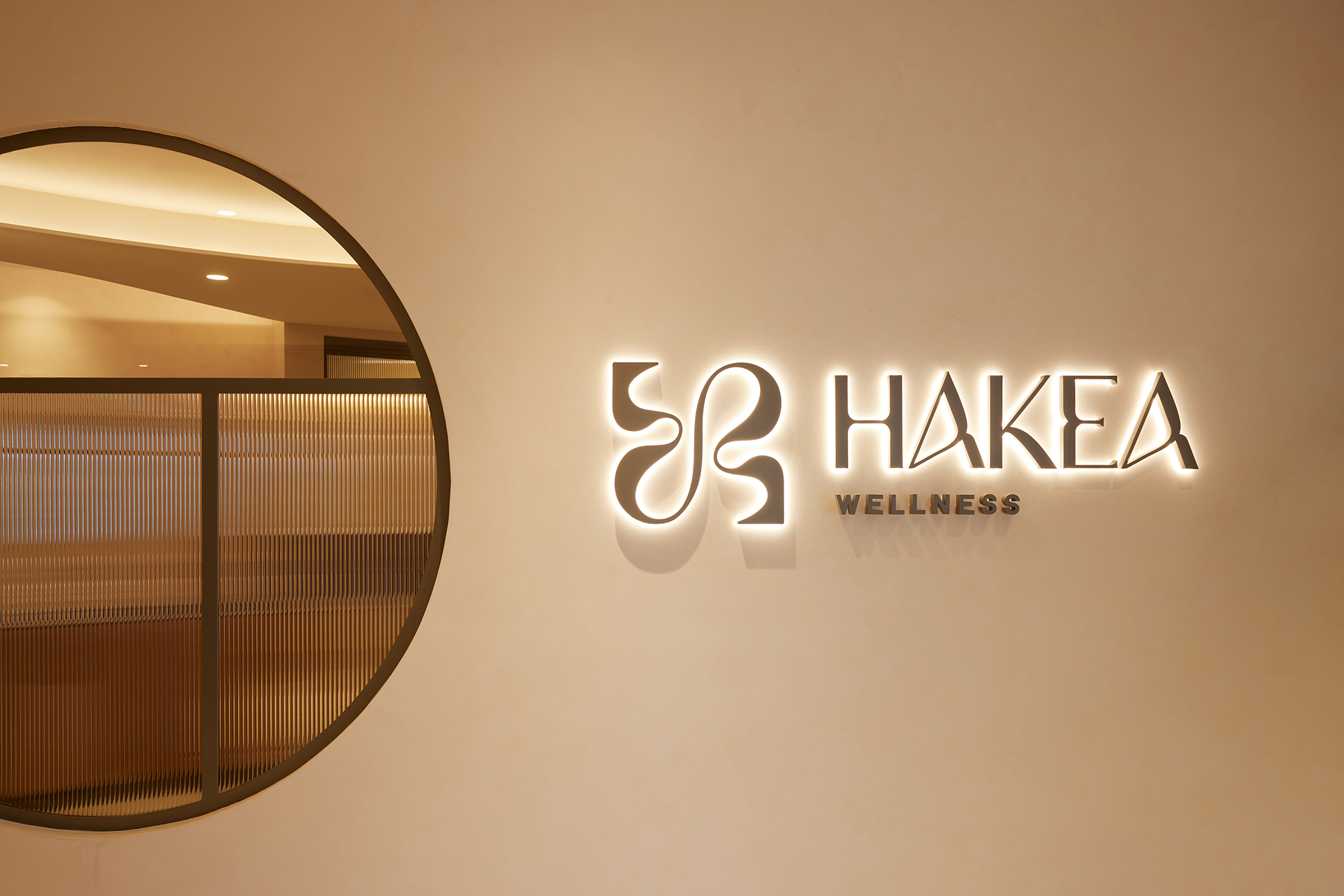 Hakea Wellness logo backlit sign, circular window, fluted glass, bronze frame, white wall, modern bright clean interior