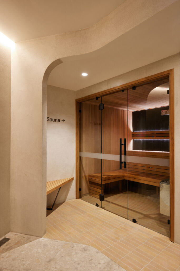 Modern wellness centre interior sauna, bronze, timber bench, earthy tones, terracotta, limewash, arched opening, glass door