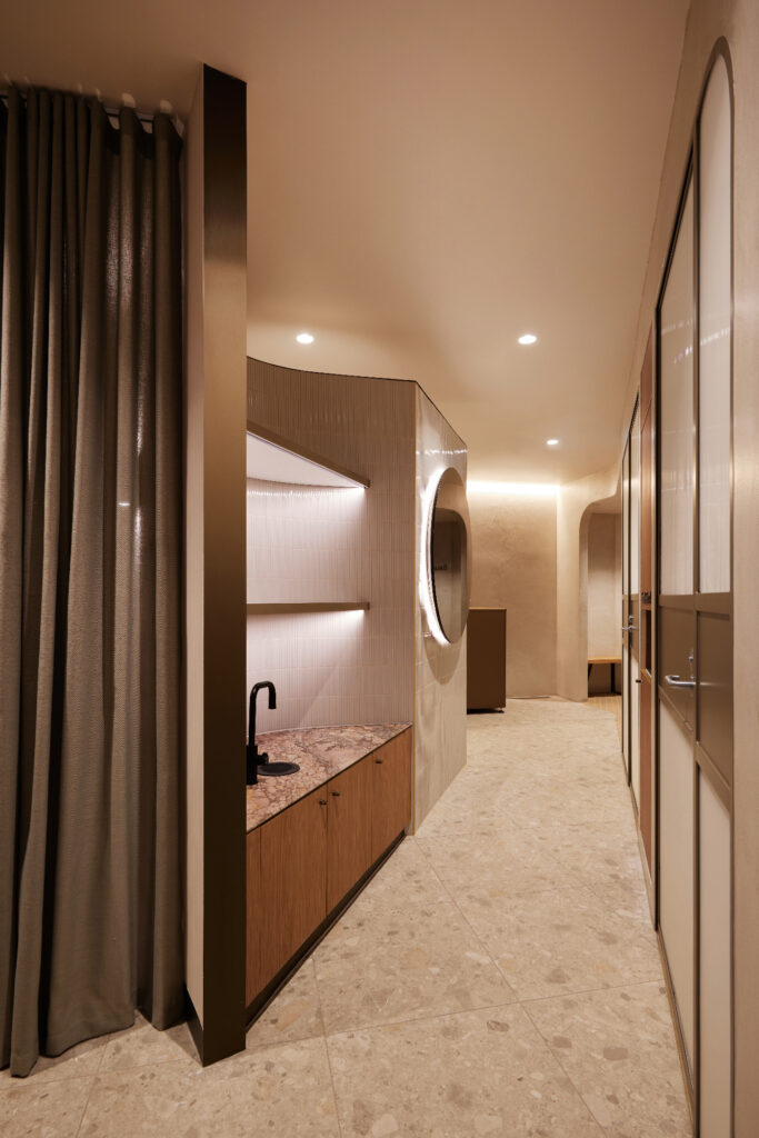 Modern, curvilinear wellness centre interior with earthy tones, marble, timber veneer, finger tiles and bronze accents.