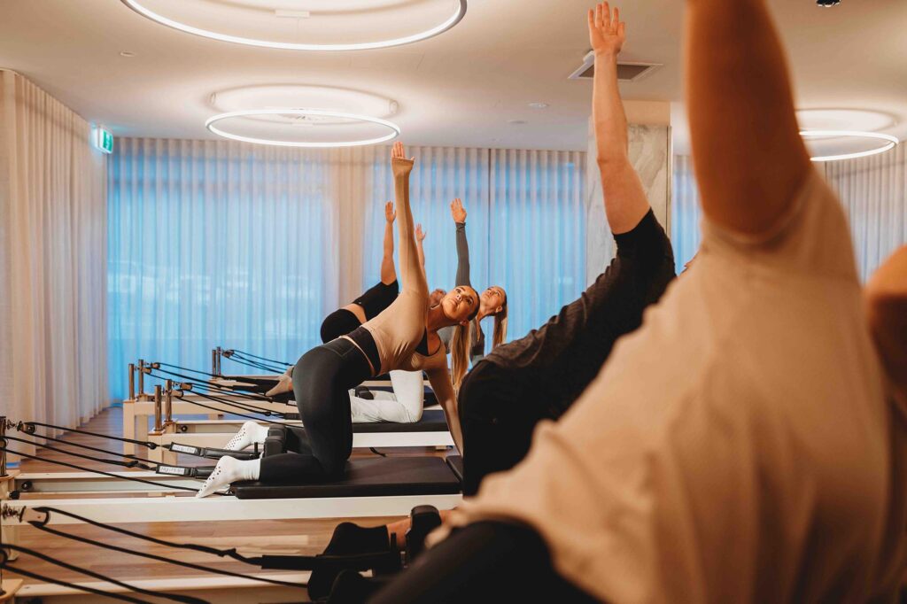People stretching doing pilates in a bright modern interior, warm earthy tones, timber floor, LED ring lights, sheer curtains
